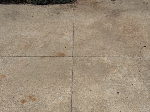 Multiple orange rust stains across a residential concrete driveway before targeted treatment